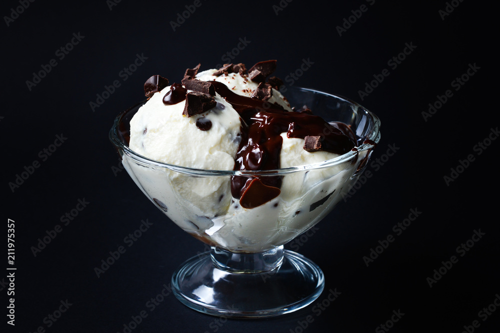 Vanilla ice cream in a white bowl with chocolate on a black background.