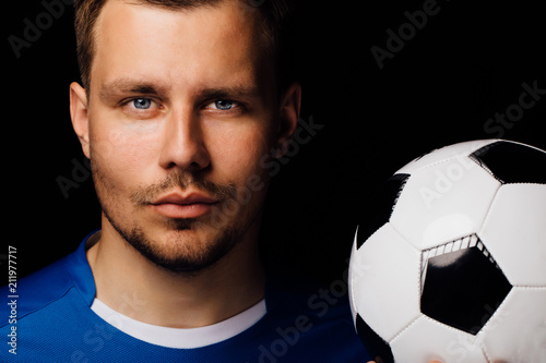 Close-up portrait of young handsome football player soccer posing on dark background.