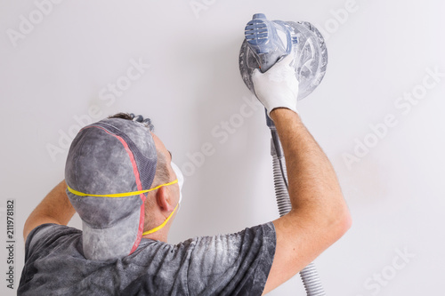 Fotografie Plasterer wearing dust mask polishes a wall with sanding machine