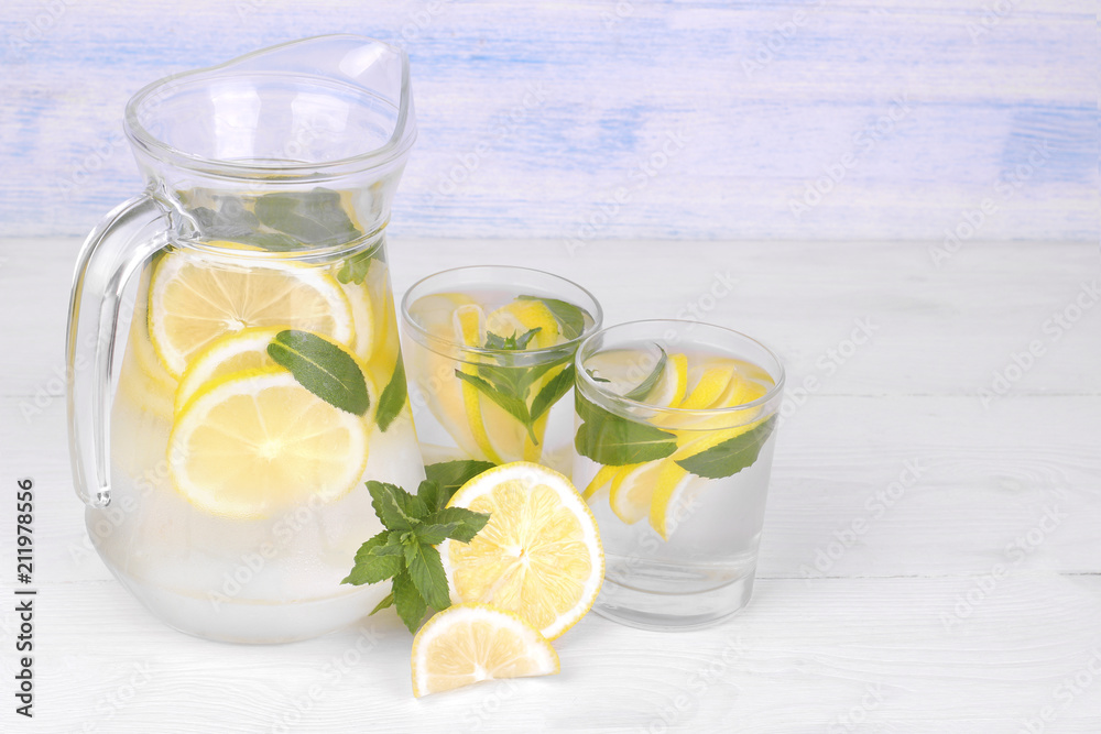 Homemade lemonade with lemon and mint in a glass jug and a glass next to fresh lemon on a white and blue wooden background...