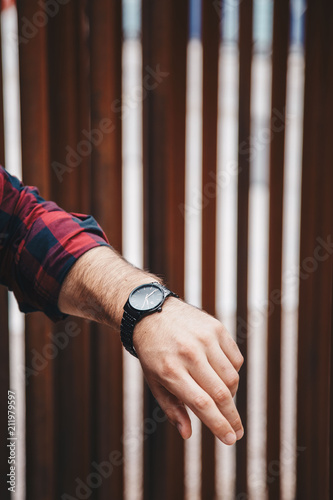 close up fashion details, young fashionable man wearing a red checked shirt and a black analog wrist watch. street style detail of an elegant clock.