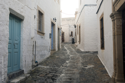 A view of a narrow street with arch and wooden windows and doors with white wall stone architecture of the island Patmos, Greece  © CoolimagesCo