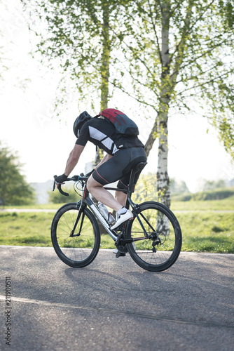 Back of a cyclist with a backpack while riding in the city on a bike. Man in sportswear and a helmet rides the city park. photo