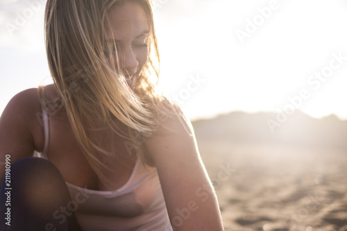 beautiful blonde model girl young woman at the beach during the sunset with sun in backlight. smile and enjoy the leisure activity alone in happiness. travel and wanderlust concept