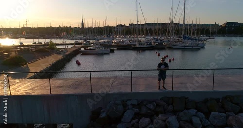 Man looking at the sea, C4k aerial tracking view around a man standing at a wharf watching boats on the baltic sea, , on a sunny summer evening dusk, in Helsinki, Uusimaa, Finland photo