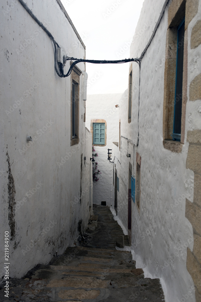 A view of a narrow street with arch and wooden windows and doors with white wall stone architecture of the island Patmos, Greece