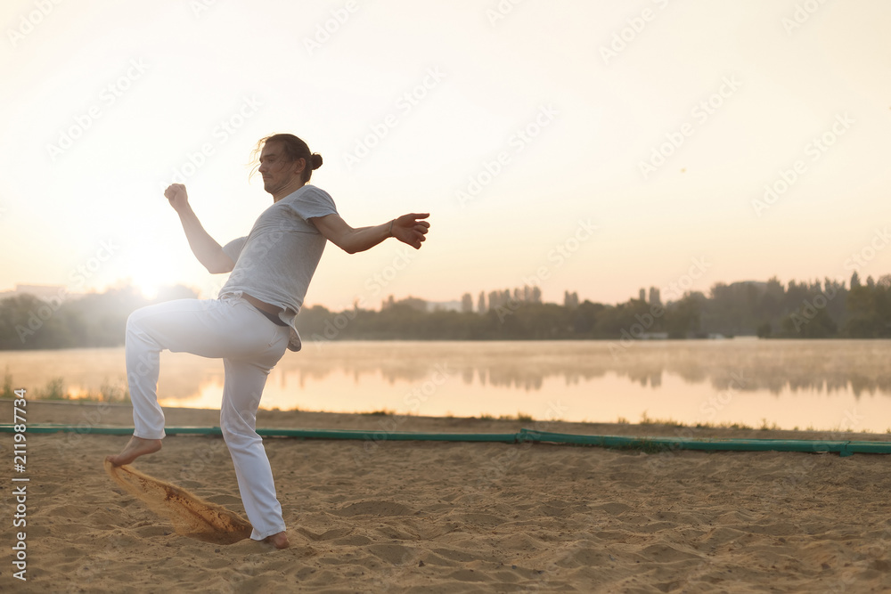 Fototapeta premium Athletic capoeira performer workout training on the beach sunris