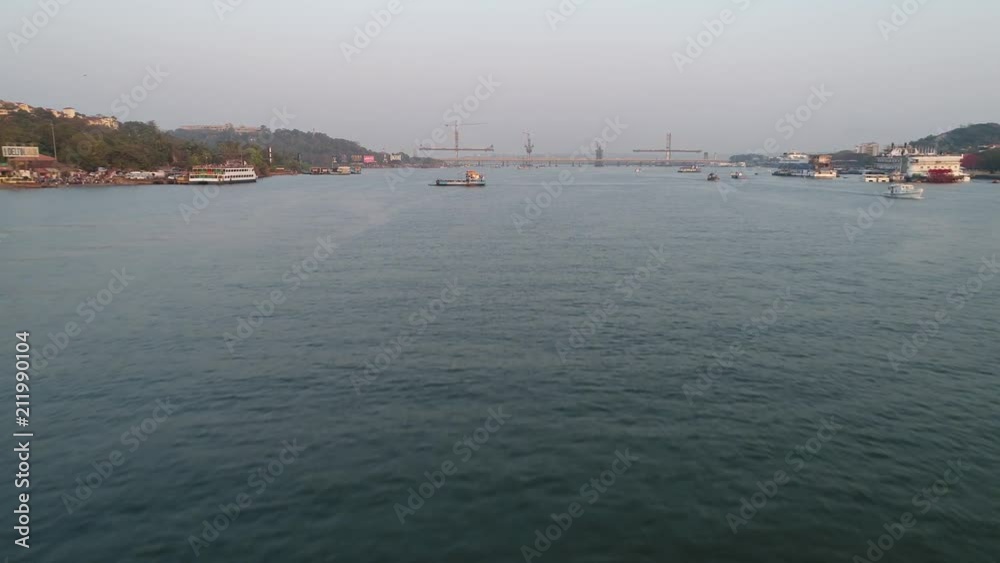 Flying camera moves along the Mandovi river in Panaji, Goa, India. Small ferryboat floats from shore to shore, big bridge on background. Aerial view. Flying camera moves along the Mandovi river in Panaji, Goa, India. Small ferryboat floats from shore to shore, big bridge on background. Aerial view.