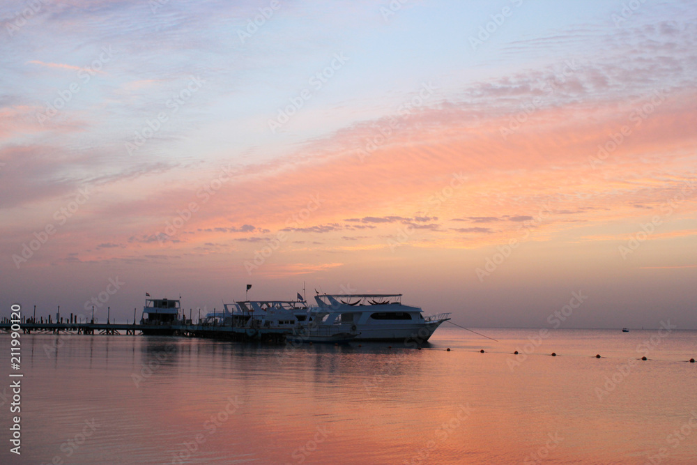 Beautiful pink sunrise on the sea. Boats on the water. Warm rays of sun light. Red sea,  Egypt.
