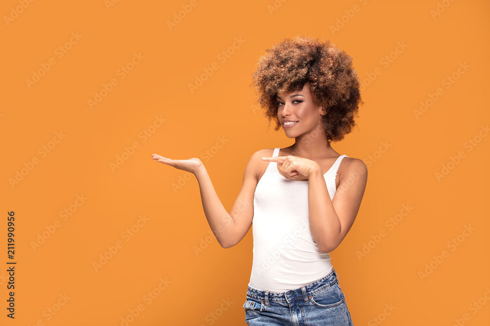 Cheerful afro woman points her fingers on yellow background. Cheerful afro woman points her fingers on yellow background.