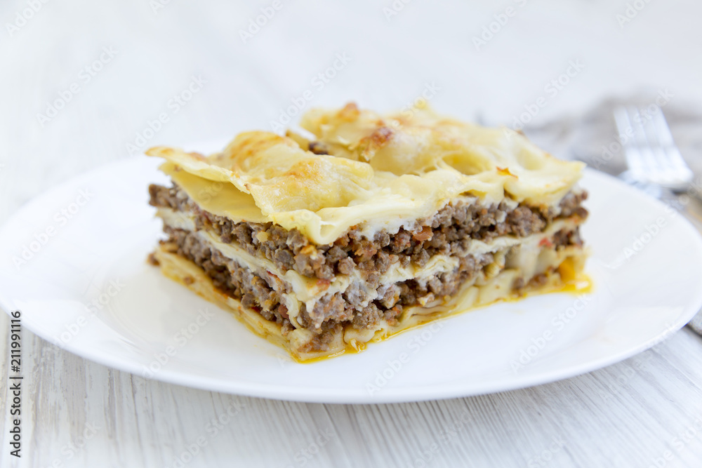 Italian beef lasagne on a white round plate, close-up. White wooden background. Side view. Italian beef lasagne on a white round plate, close-up. White wooden background. Side view.