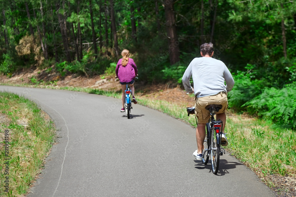 Loving married couple riding on bicycles. A man in beige shorts and a woman in a purple shirt. View from the back. Bike ride in the nature on a sunny summer day