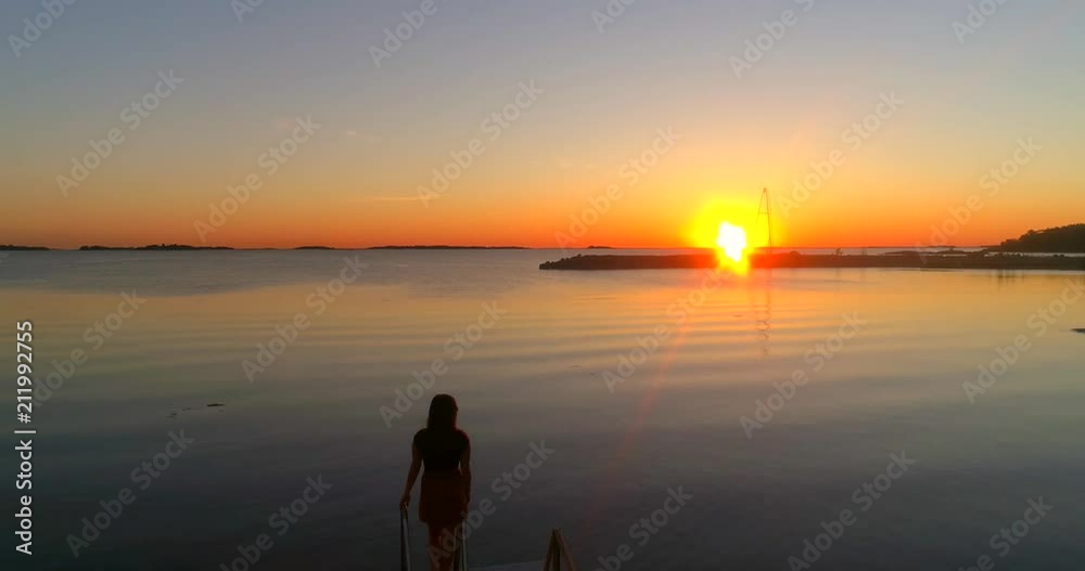 Woman looking at the sea, C4K aerial backward view over a girl enjoying the sunset, at a wharf, on a beach at the baltic sea, on a sunny summer evening dusk, Hanko, Finland Woman looking at the sea, C4K aerial backward view over a girl enjoying the sunset, at a wharf, on a beach at the baltic sea, on a sunny summer evening dusk, Hanko, Finland