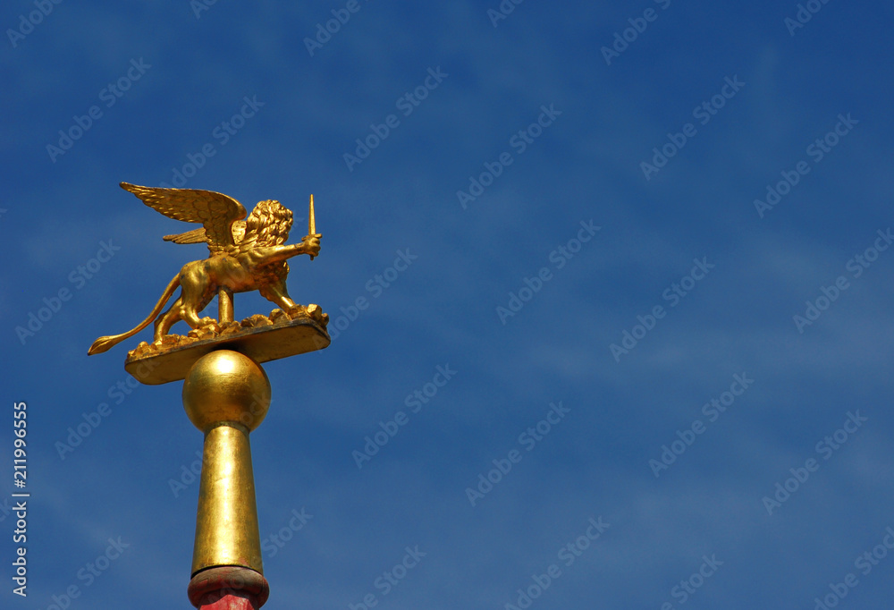 Saint Mark Winged Lion golden statuette wielding a sword against blue sky, a symbol of the Old Venice Republic at war (with copy space)