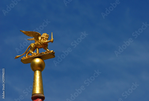 Saint Mark Winged Lion golden statuette wielding a sword against blue sky, a symbol of the Old Venice Republic at war (with copy space)