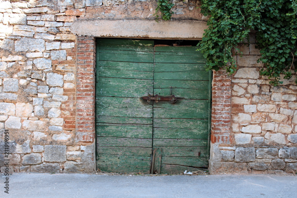 Old green wooden garage doors with heavy metal lock and brick frame inside traditional stone wall Old green wooden garage doors with heavy metal lock and brick frame inside traditional stone wall