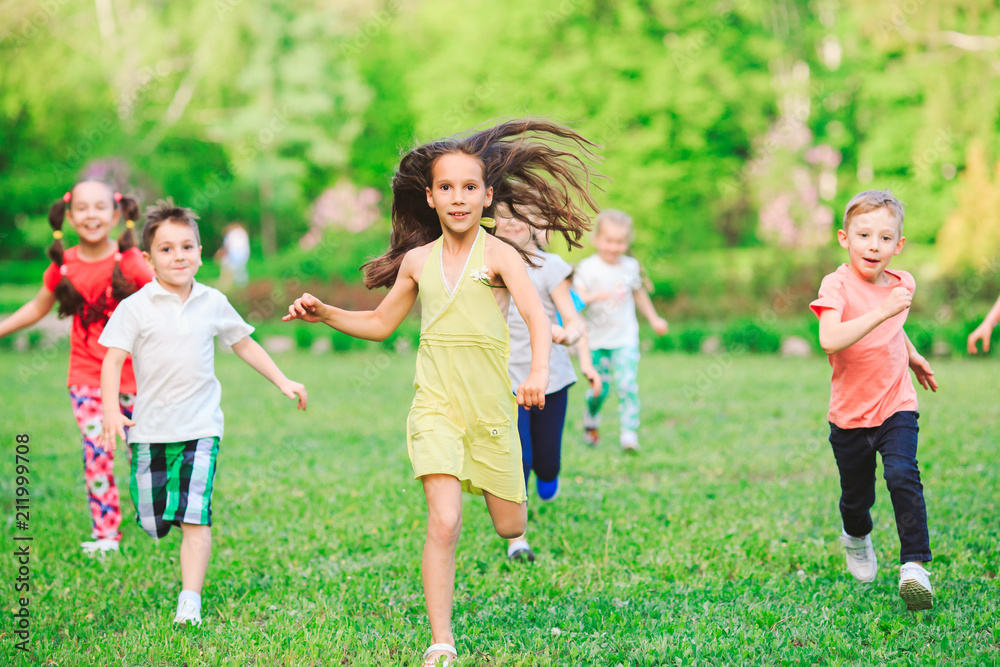 Many different kids, boys and girls running in the park on sunny summer day in casual clothes