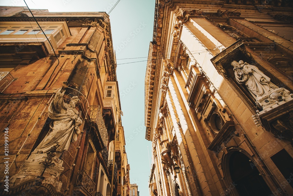 Naklejka premium Traditional Maltese street with corners of houses, decorated with statues of saint in Valletta, Capital city of Malta. Building facade