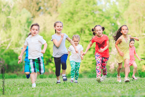 Many different kids, boys and girls running in the park on sunny summer day in casual clothes