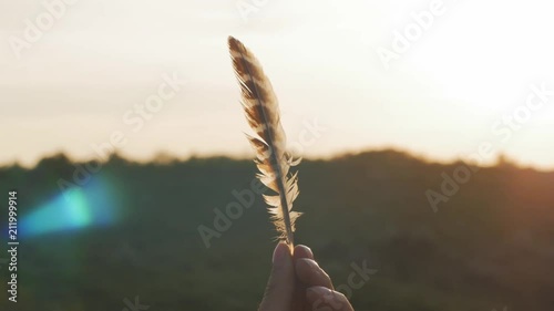 Woman with a bird's feather in hand against the beautiful setting sun, freedom concept 