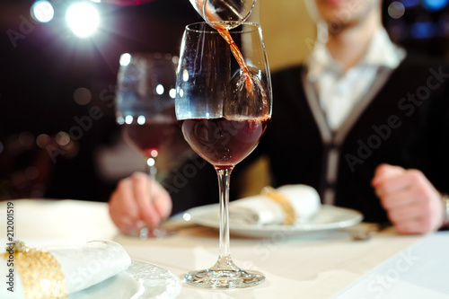 Waiter pouring red wine in a glass at a restaurant table