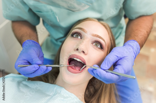 Close-up picture of young woman sitting in the dentist s chair with opened mouth at dentist s office while having examination.