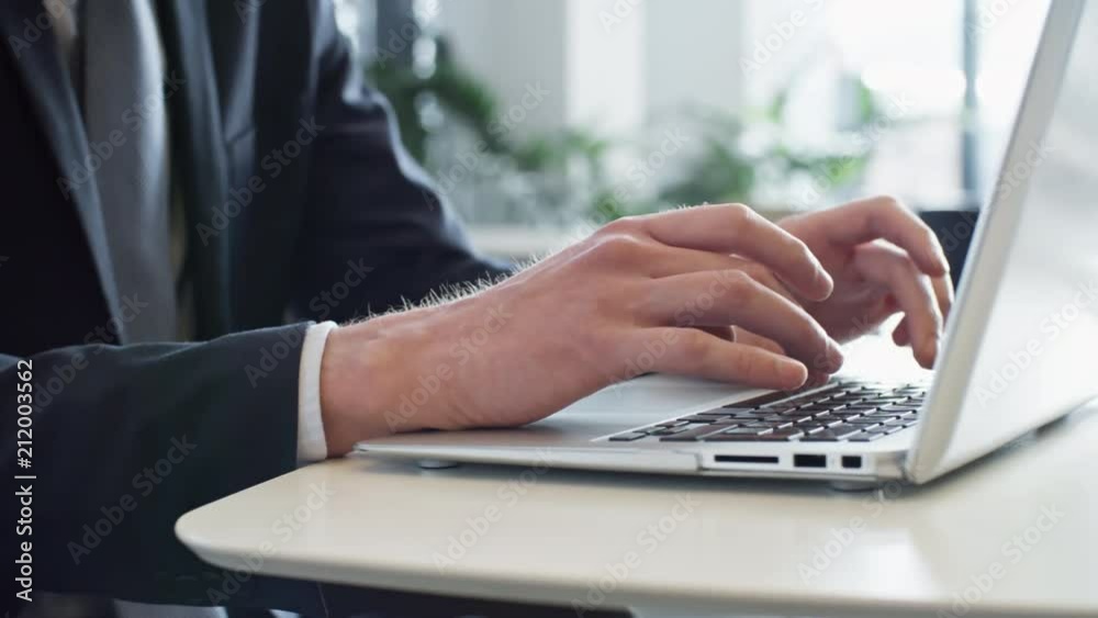 Pan closeup shot of hands of unrecognizable businessman typing on laptop while working in the office