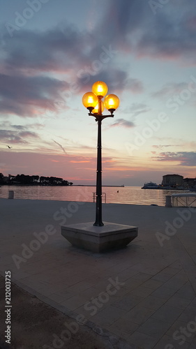 Single old baroque style street lamp with bright yellow light near sea at sunset