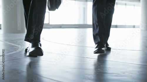 Closeup low angle shot of legs of two unrecognizable businessmen walking towards the camera in hall of office building photo