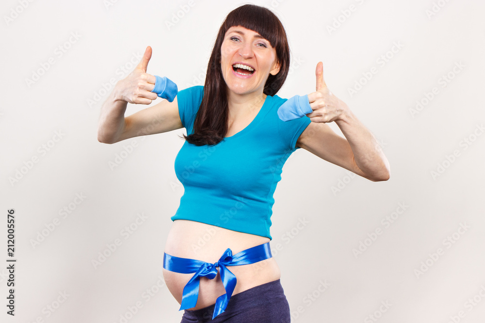 Smiling pregnant woman with baby gloves and blue ribbon, concept of expecting for newborn Smiling pregnant woman with baby gloves and blue ribbon, concept of expecting for newborn