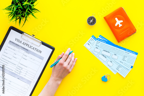 Hand fills visa application form. Form near glasses, pen, passport cover with airplane signand airplane tiskets on yellow background top view copy space photo