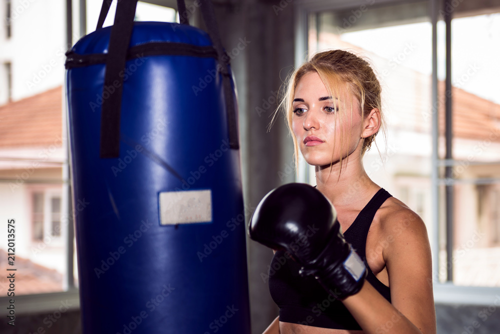 Young female punching a bag with boxing glove.
