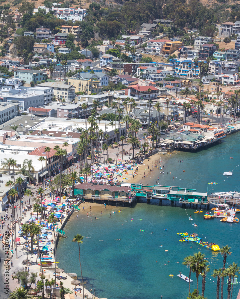 Catalina Island vacation resort, Avalon, California, aerial view of green pleasure pier, calm ocean bay view of colorful houses, beach umbrellas and sunbathers