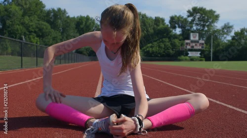 Teen girl stretches cross legged on a track