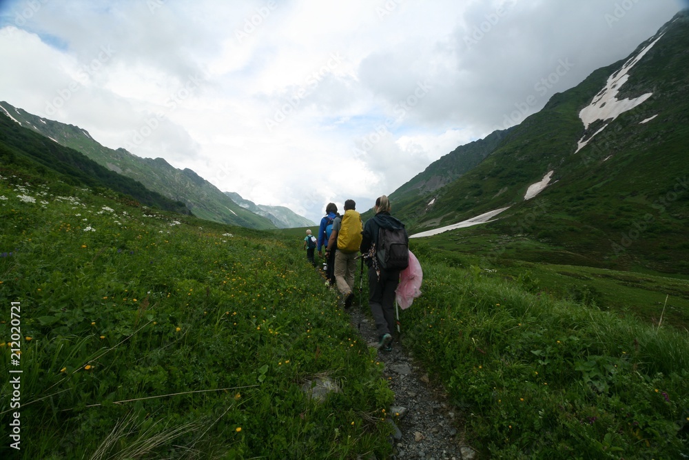 Tourists go along the trail of flowering meadows in the Caucasus mountains