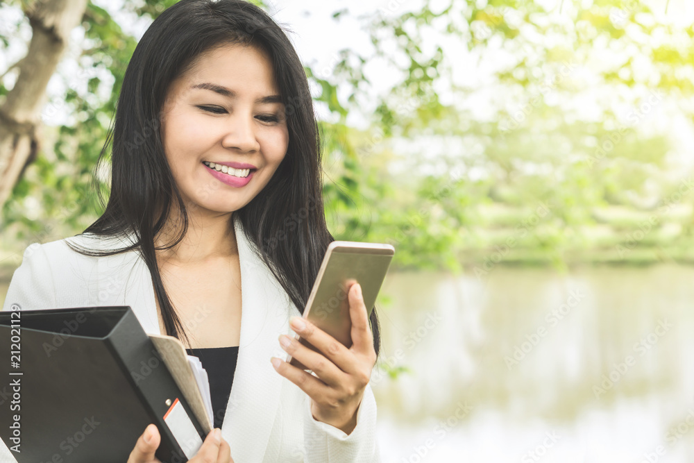 happy Asian business woman outdoors smiling at smart phone in hand happy Asian business woman outdoors smiling at smart phone in hand