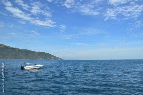 speed white boat at the entrance to the open sea, against the background of the coastline of the island, sky and clouds