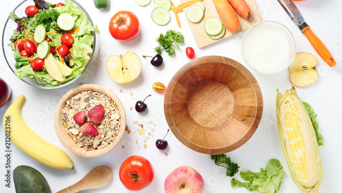 Top view of empty wooden bowl, mixed vegetables salad, muesli and fresh fruits on white background.