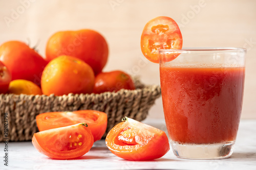 Glass of tomato juice and fresh tomatoes on marble table.