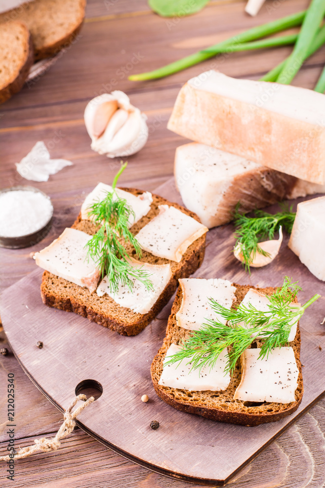 Sandwiches from rye bread, salted bacon and dill on a cutting board on a wooden table Sandwiches from rye bread, salted bacon and dill on a cutting board on a wooden table