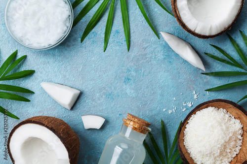 Blue background with set of organic coconut products for spa treatment, cosmetic or food ingredients. Oil, water and shavings top view. Flat lay.