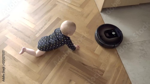 Baby boy versus Robotic vacuum cleaner on wooden fioor view from above photo