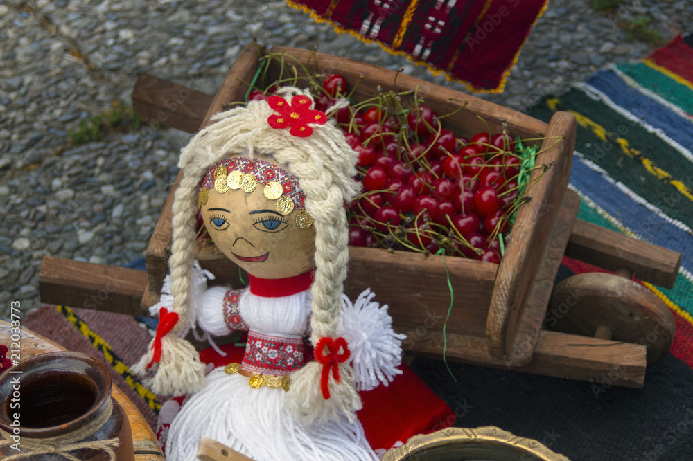 Doll in a typical Bulgarian folk costume to a decorative cart with cherry.Kustendil, Bulgaria.
