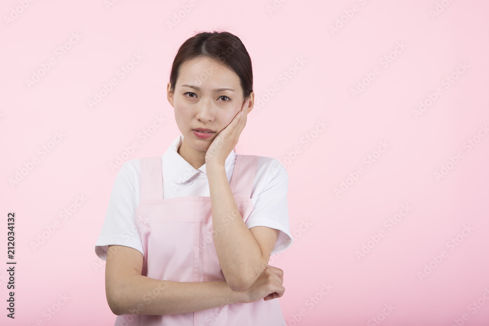 頬に手を当てて痛そうな顔をする白衣とエプロンを着た女性 頬に手を当てて痛そうな顔をする白衣とエプロンを着た女性