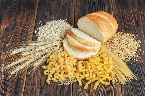 Foods high in carbohydrate on wooden background. Loaf, pasta, pearl barley and oats.