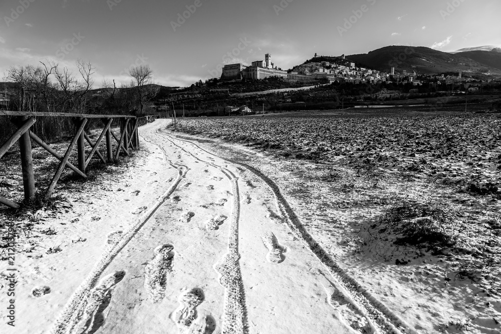 View of Assisi town (Umbria) in winter, with a field covered by snow and sky with white clouds
