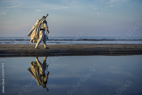 Portrait of assassin in white costume with the sword at the sea. He is posing...