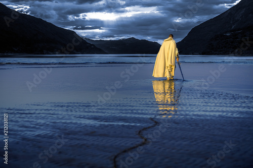 Portrait of assassin in white costume with the sword at the sea. He is posing...