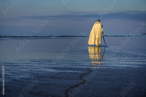 Portrait of assassin in white costume with the sword at the sea. He is posing...