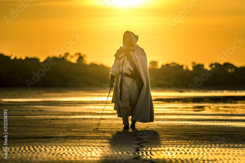 Portrait of assassin in white costume with the sword at the sea. He is posing...